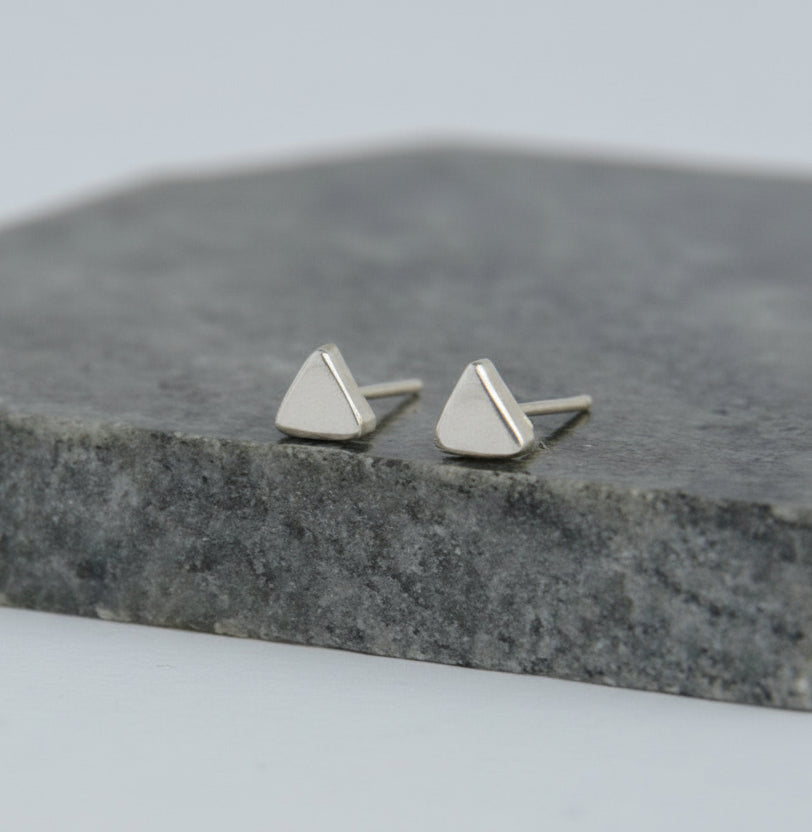 Pair of silver triangle stud earrings on a gray stone surface