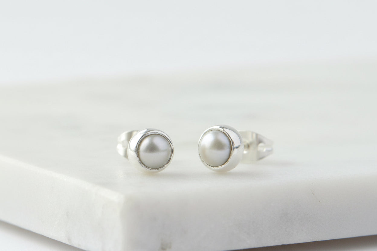 Pair of silver earrings with pearl-like stones on a marble surface