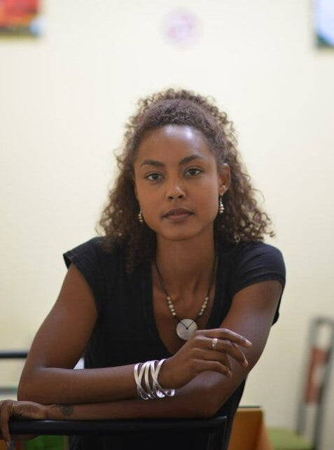 Woman with curly hair wearing a black top and multiple bracelets, sitting indoors.